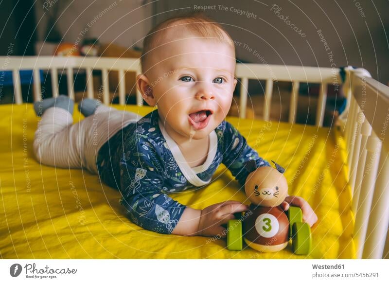 Portrait of baby boy with wooden toy lying in his crib Cot children's bed portrait portraits baby boys male beds babies infants people persons human being