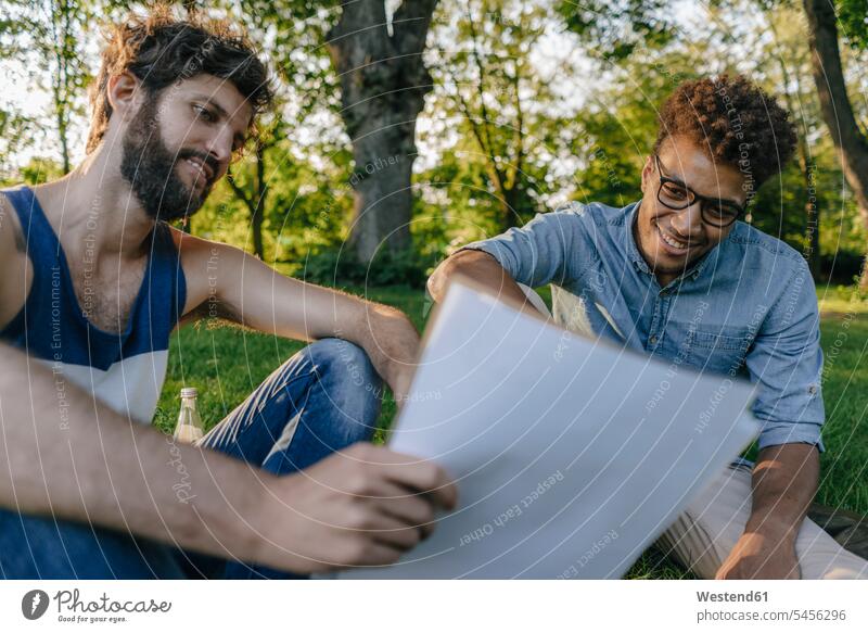 Two friends sitting in a park discussing papers Seated parks documents discussion man males friendship Adults grown-ups grownups adult people persons