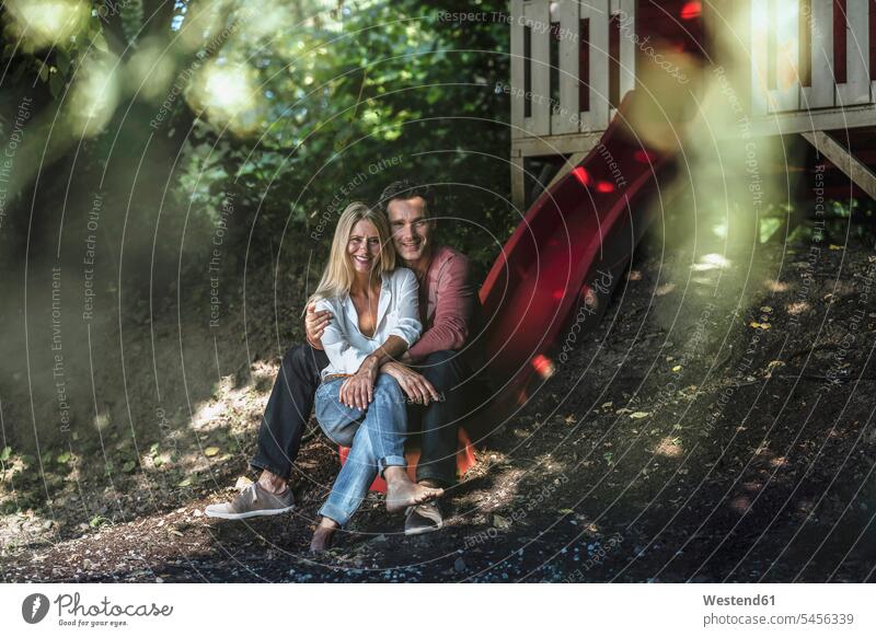 Happy couple sitting on slide of garden shed in the woods Seated smiling smile forest forests happiness happy twosomes partnership couples Chute