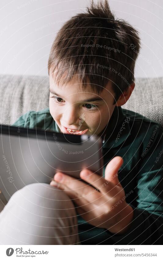 Portrait of laughing boy sitting on the couch in the living room using tablet use digitizer Tablet Computer Tablet PC Tablet Computers iPad Digital Tablet