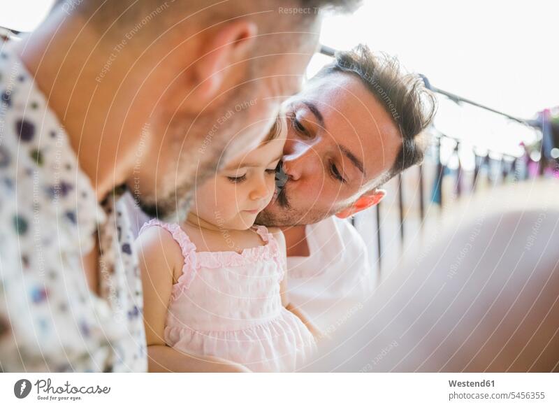 Affectionate gay couple with daughter on balcony happiness happy daughters gay men gay man homosexual men homosexual man kissing kisses twosomes partnership