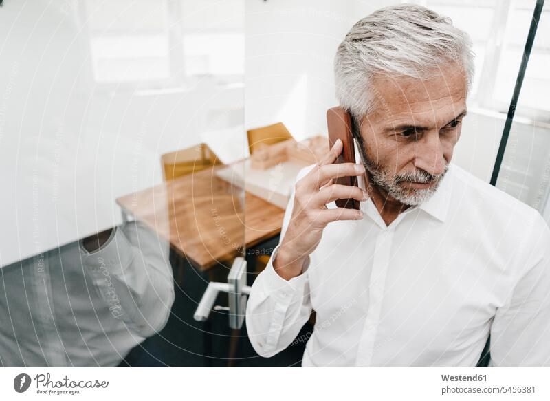 Mature businessman on the phone in office thinking offices office room office rooms mobile phone mobiles mobile phones Cellphone cell phone cell phones