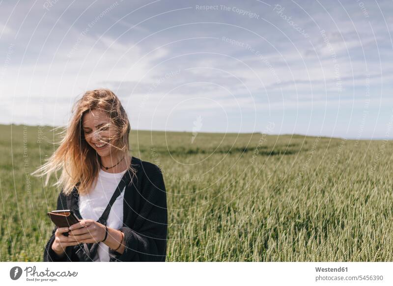 Young woman using smartphone, standing in field Smartphone iPhone Smartphones smiling smile texting sending mobile phone mobiles mobile phones Cellphone