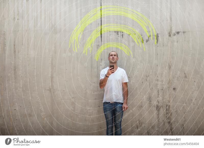 Man holding cell phone with yellow chalk wifi sign above his head symbol symbols mobile phone mobiles mobile phones Cellphone cell phones wall walls Wifi Wi-Fi
