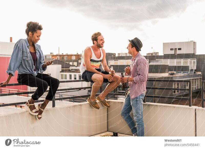 Three friends socializing on a rooftop party celebrating celebrate partying Party Parties Fun having fun funny drinking roof terrace deck Beer Beers Ale