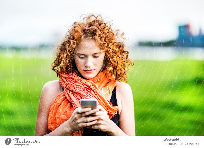 Portrait of young woman with curly red hair looking at cell phone females women portrait portraits Adults grown-ups grownups adult people persons human being