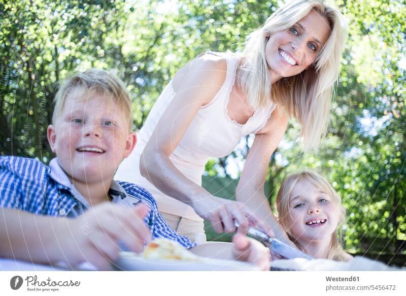 Smiling mother with children at garden table smiling smile daughter daughters son sons manchild manchildren mommy mothers mummy mama family families people