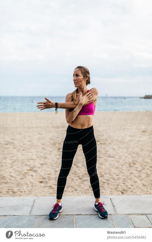 Young woman stretching and warming up for training at the beach warm up females women standing beaches exercising exercise practising sport sports Adults