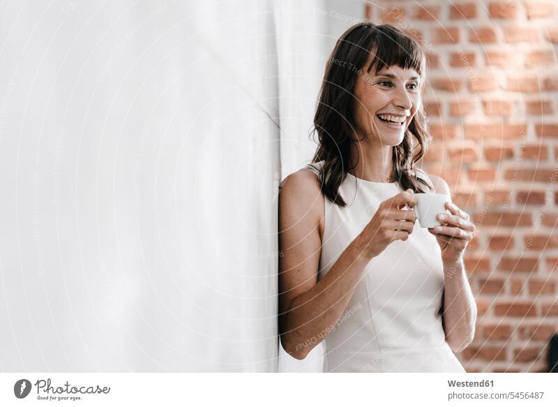 Woman drinking coffee in office, leaning against wall standing Coffee woman females women Drink beverages Drinks Beverage food and drink Nutrition Alimentation
