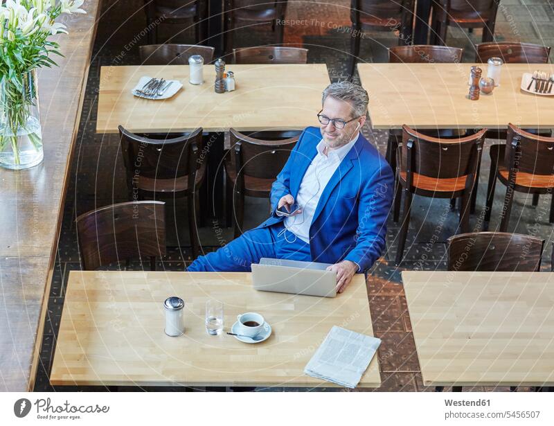 Mature businessman in cafe with laptop, cell phone and earbuds Laptop Computers laptops notebook Businessman Business man Businessmen Business men hearing