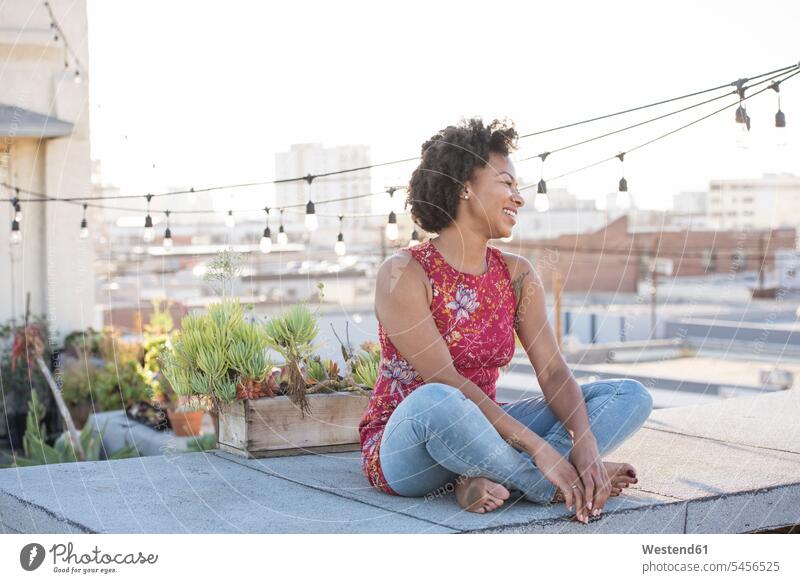 Young woman sitting on rooftop terrace, enjoying the sun cross-legged tailor seat thinking Seated roof terrace deck relaxation relaxing females women Adults