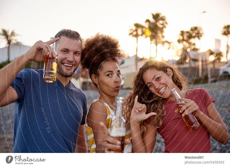 Three friends with beer bottles having fun on the beach at sunset beaches Beer Beers Ale Alcohol alcoholic beverage Alcoholic Drink Alcoholic Drinks