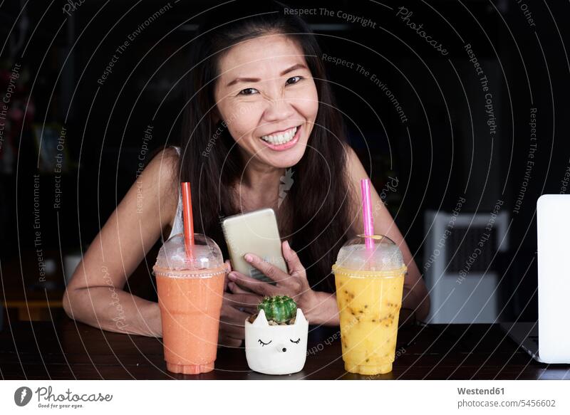 Portrait of happy woman with cell phone and smoothies Smoothies portrait portraits females women happiness smiling smile Drink beverages Drinks Beverage