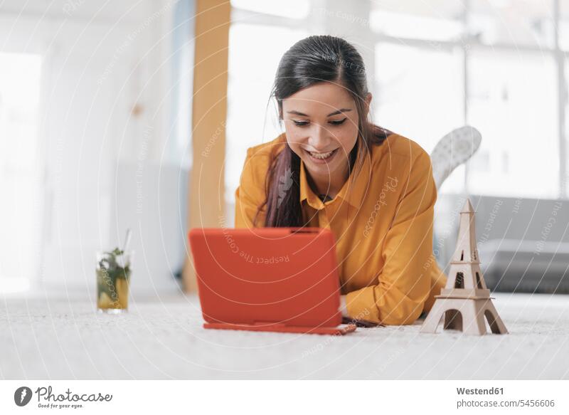 Young woman with model of the Eiffel Tower planning trip to Paris females women booking lying laying down lie lying down carpet carpets rug rugs laptop