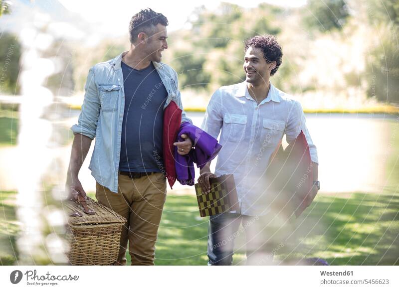 Two friends walking in park with picnic basket and chessboard smiling smile man men males friendship Adults grown-ups grownups adult people persons human being