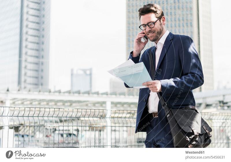 Businessman standing on parking level, making a call with documents in hands Smartphone iPhone Smartphones on the phone telephoning On The Telephone calling