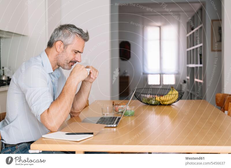 Smiling man drinking coffee and using laptop in home office smiling smile working from home home business at home men males Coffee Businessman Business man