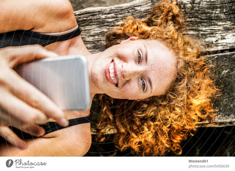 Portrait of redheaded young woman lying on bench using cell phone portrait portraits females women Adults grown-ups grownups adult people persons human being