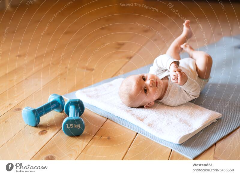 Baby at home lying on mat next to dumbbells baby infants nurselings babies laying down lie lying down Hand Weight Hand Weights people persons human being humans