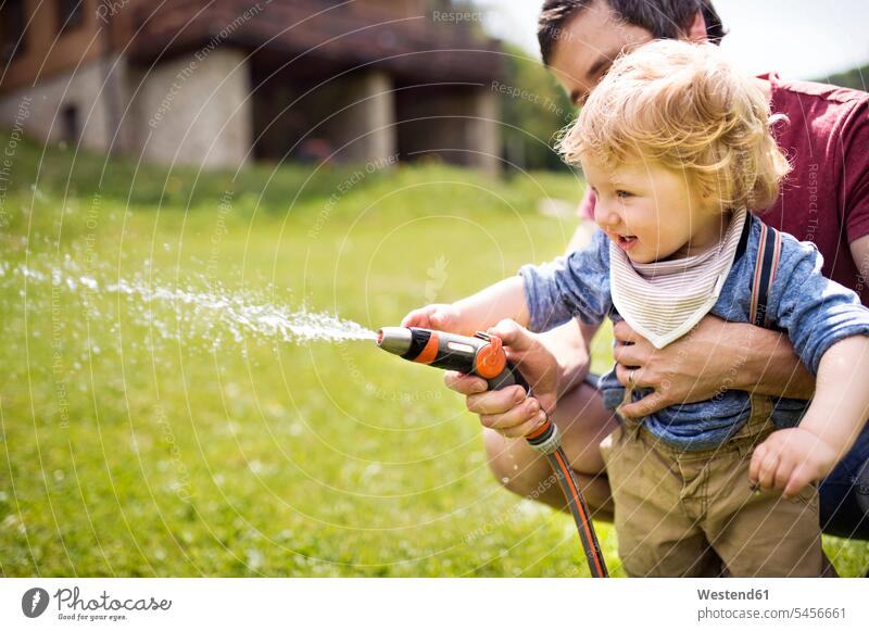Little boy with his father watering the lawn son sons manchild manchildren hose hoses pa fathers daddy dads papa garden gardens domestic garden family families