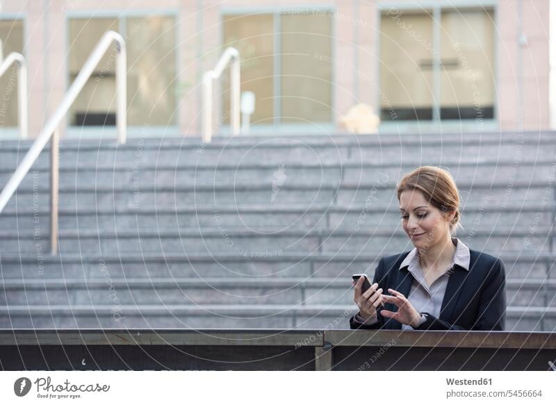 Businesswoman checking cell phone outdoors businesswoman businesswomen business woman business women business people businesspeople business world business life