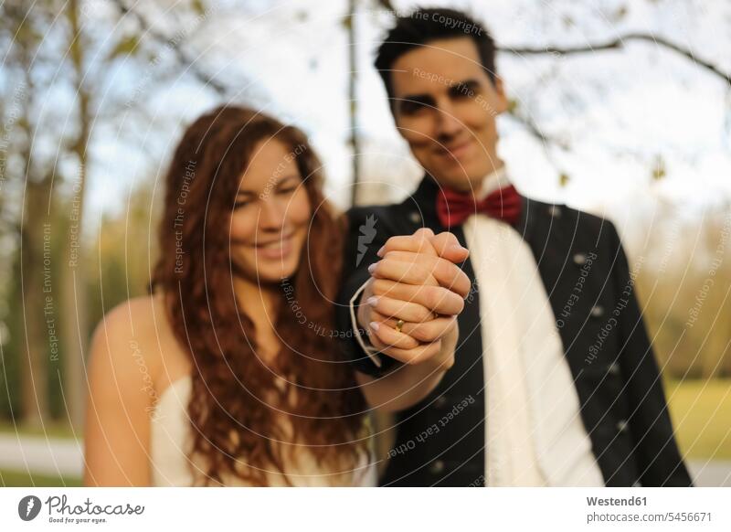 Happy bridal couple standing in park, holding hands, showing wedding ring hand in hand twosomes partnership couples Wedding Bands wedding rings happiness happy
