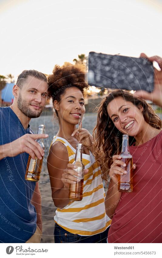 Three friends with beer bottles taking selfie on the beach Beer Beers Ale beaches Selfie Selfies Alcohol alcoholic beverage Alcoholic Drink Alcoholic Drinks
