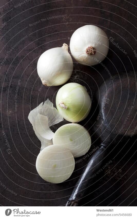 Sliced and whole white onions on rusty ground sliced onion skin onion skins wooden spoon wooden spoons Brown Background brown dark background Allium Cepa half
