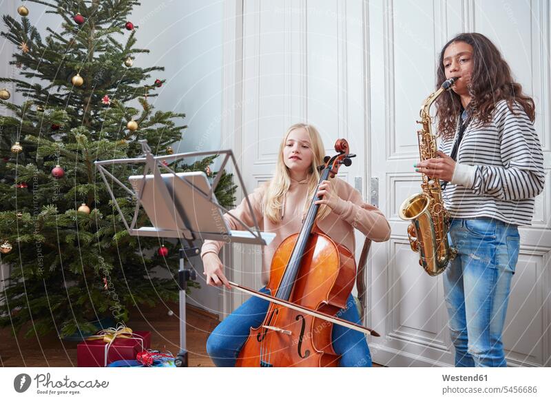 Two girls playing cello and saxophone at Christmas tree females music Christmas trees child children kid kids people persons human being humans human beings