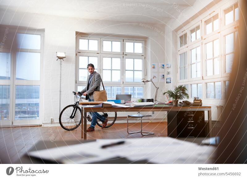Man with bicycle in a modern informal office man men males bikes bicycles offices office room office rooms Businessman Business man Businessmen Business men