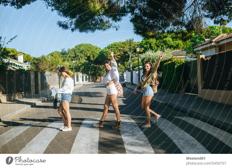 Three friends crossing pedestrian crossing showing victory sign V sign v-sign female friends zebra crossing walking going road streets roads Hand Sign