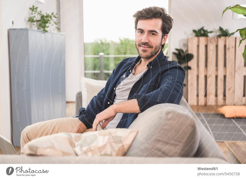 Young man sitting on couch at home, smiling settee sofa sofas couches settees comfortable amenities amenity independence independent confidence confident