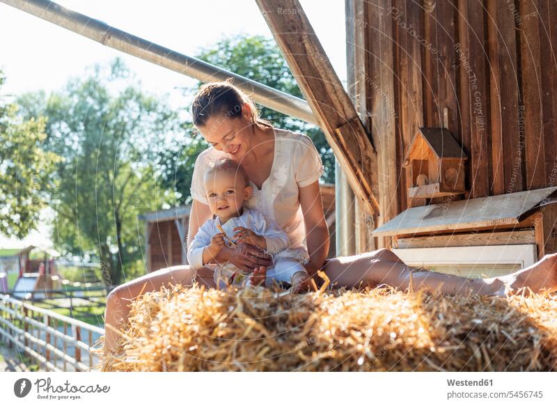 Happy mother and little daughter sitting in straw in a barn mommy mothers ma mummy mama happiness happy daughters Seated Straw parents family families people