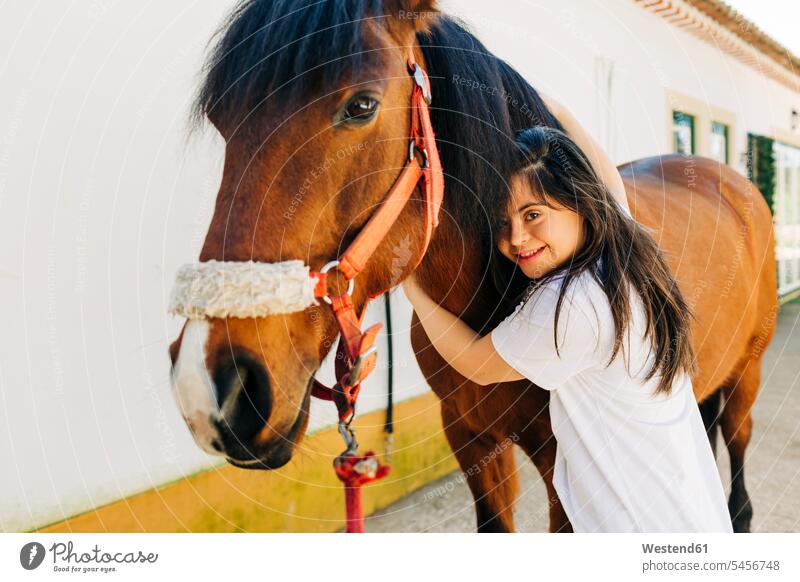 Teenager with down syndrome taking care of horse and preparing horse to ride hold cuddle snuggle snuggling smile embrace Embracement hug hugging delight