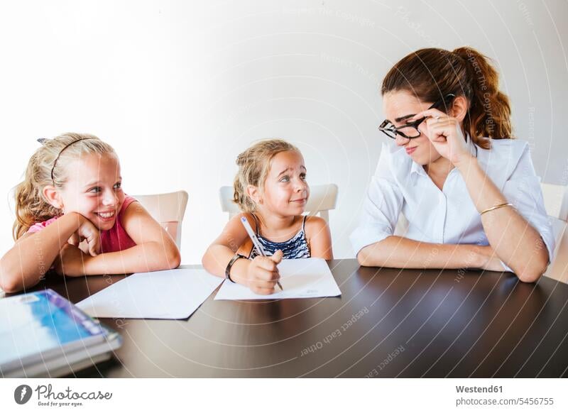 Tacher sitting at desk with two schoolgirls writing on paper human human being human beings humans person persons caucasian appearance caucasian ethnicity