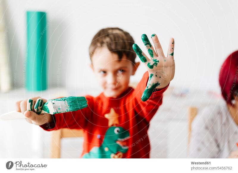 Boy showing a brush in one hand and the other painted green while doing crafts at home human human being human beings humans person persons caucasian appearance