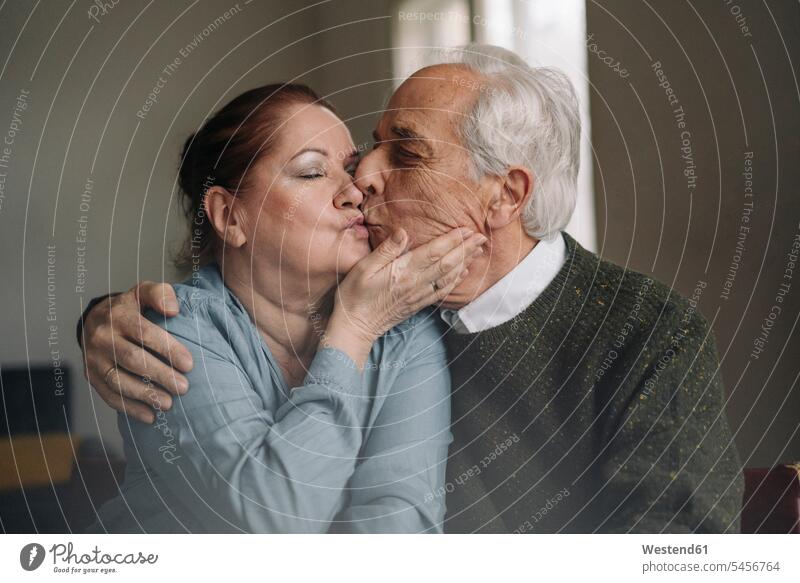 Senior couple kissing at home Seated sit embrace Embracement hug hugging relax relaxing relaxation delight enjoyment Pleasant pleasure indulgence indulging