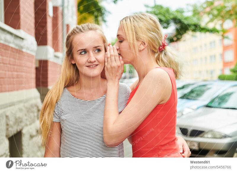 Two young women in the city whispering woman females female friends town cities towns together Adults grown-ups grownups adult people persons human being humans