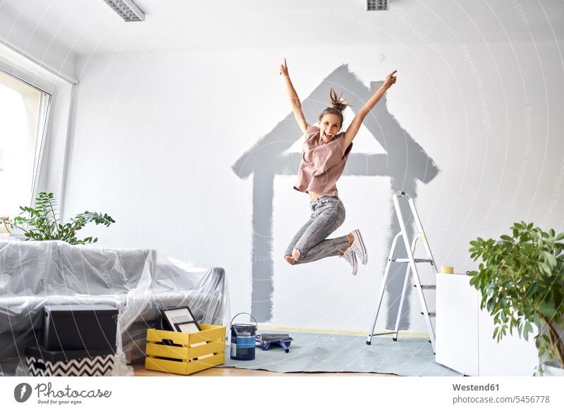 Carefree woman with hand raised jumping against wall at home color image colour image indoors indoor shot indoor shots interior interior view Interiors day
