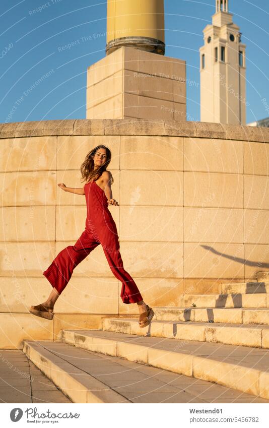 Spain, Barcelona, Montjuic, young woman wearing red jumpsuit jumping on stairs Leaping stairway females women building buildings colour colours Adults grown-ups