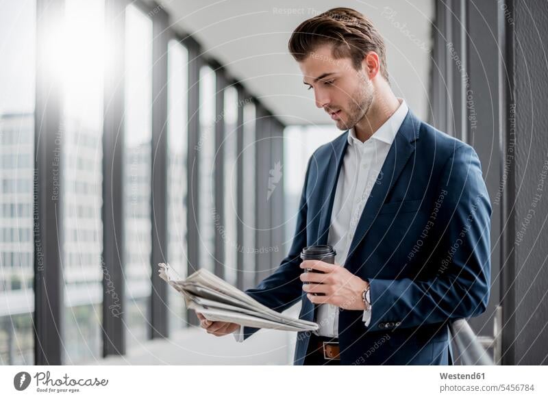 Young businessman standing in a passageway with takeaway coffee and newspaper Coffee newspapers Businessman Business man Businessmen Business men Drink