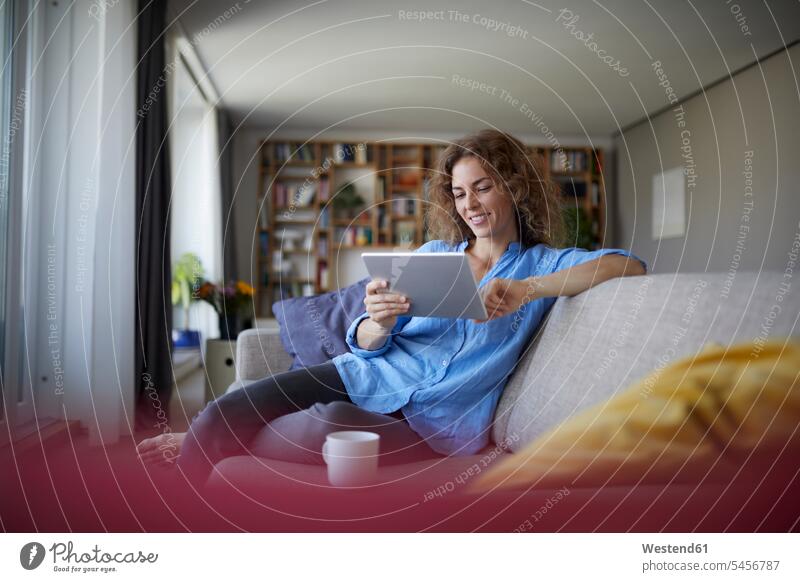 Woman using digital tablet while sitting on sofa at home color image colour image indoors indoor shot indoor shots interior interior view Interiors day