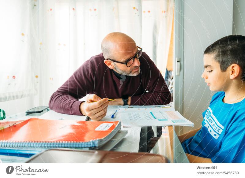 Father explaining son sitting at desk during homeschooling color image colour image Home Interior Home Interiors domestic space Homeschooling home schooling
