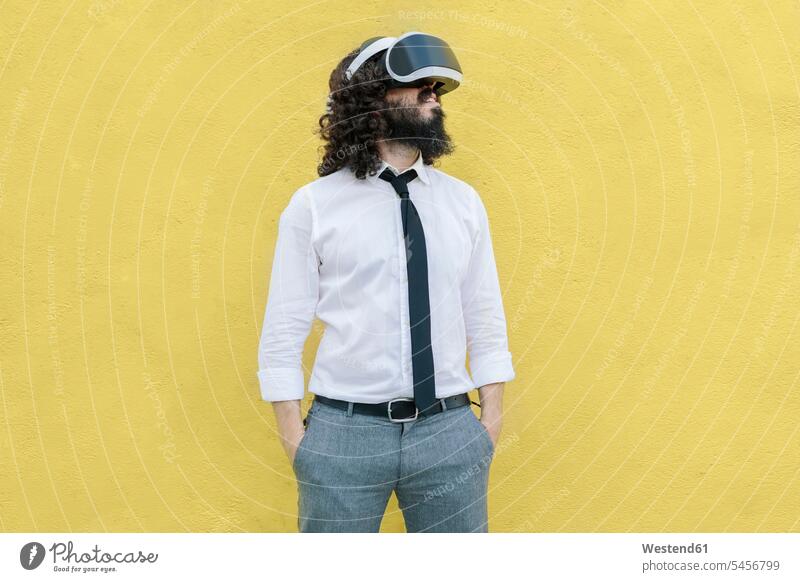 Business wearing virtual reality eyeglasses standing with hands in pockets against yellow wall color image colour image outdoors location shots outdoor shot