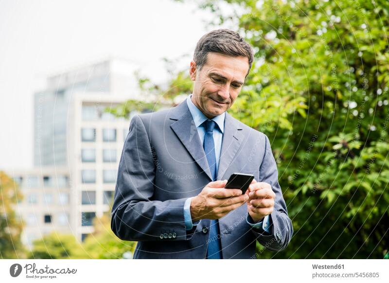 Businessman using cell phone in city park parks Business man Businessmen Business men town cities towns mobile phone mobiles mobile phones Cellphone cell phones