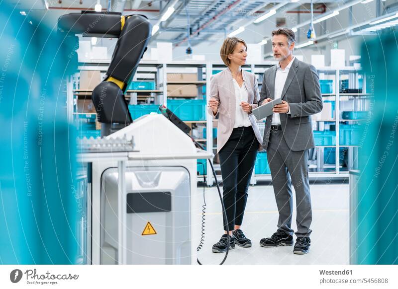 Businessman and businesswoman talking in a modern factory hall business life business world business person businesspeople associate associates