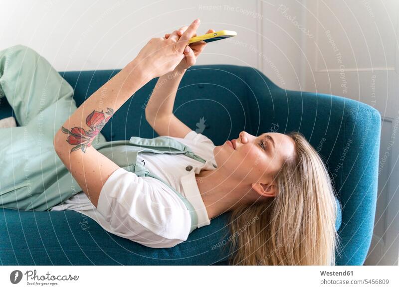 Young woman lying on couch using cell phone human human being human beings humans person persons caucasian appearance caucasian ethnicity european 1