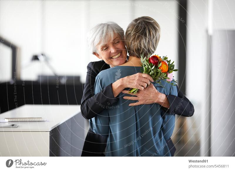 Happy senior businesswoman with bunch of flowers hugging colleague in office generation Occupation Work job jobs profession professional occupation