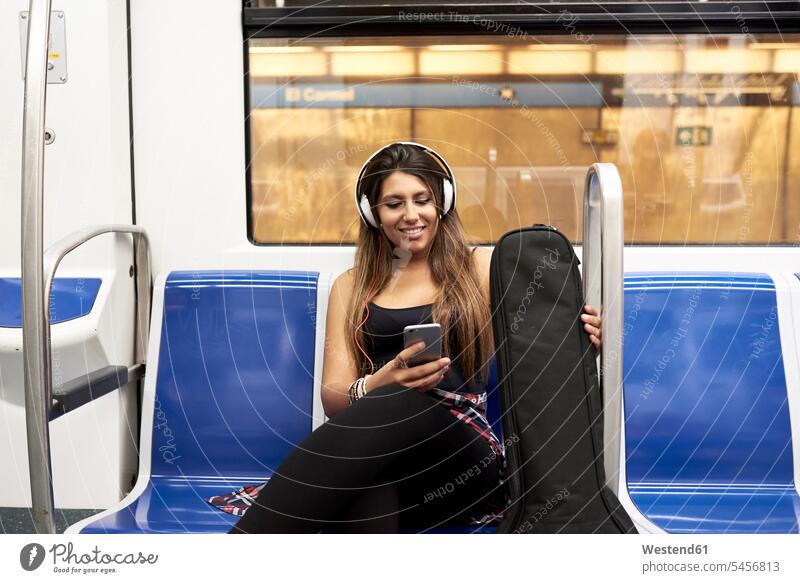 Portrait of smiling woman with guitar and headphones looking at cell phone in underground train females women portrait portraits smile eyeing Smartphone iPhone
