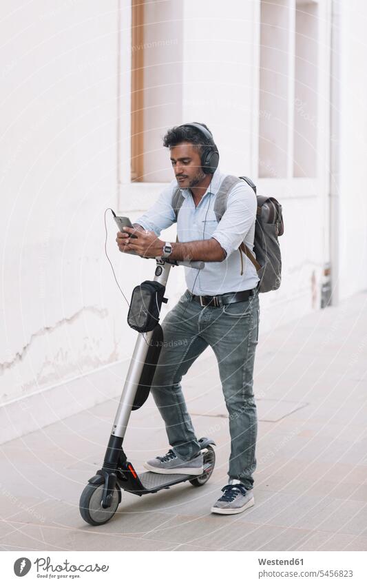 Casual businessman with headphones, smartphone and e-scooter in the city human human being human beings humans person persons Indian 1 one person only